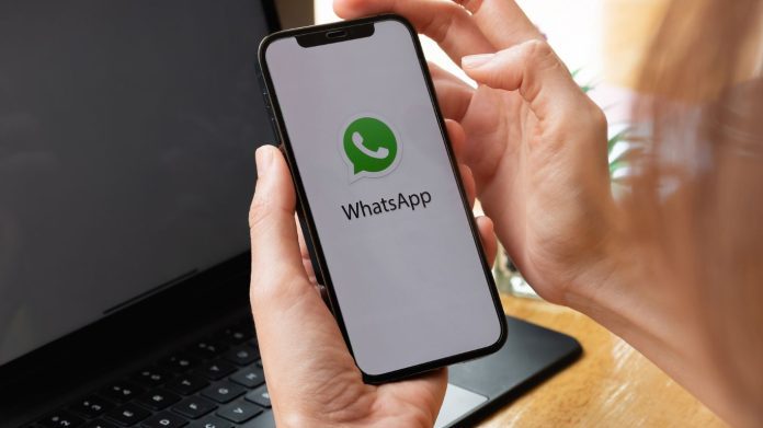 whatsapp launcher showing on mobile phone in someone hands in front of laptop